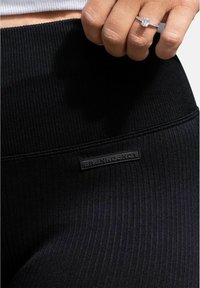 Svarta ribbade leggings med en bred linning, gjorda av ett strukturerat material och med en liten rektangulär varumärkesetikett sydd på sidan.