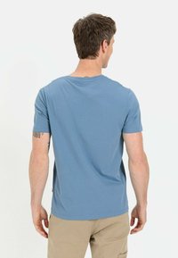 Blaues Kurzarm-T-Shirt aus weichem Stoff mit Rundhalsausschnitt und geradem Saum, mit einem Etikett an der unteren linken Seite.