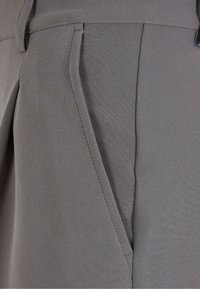 Gros plan sur un pantalon gris sur mesure mettant en avant la poche latérale, la passants de ceinture et les détails des coutures.