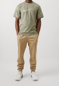 Oliwkowa bawełniana koszulka z białym logo Nike, w połączeniu z beżowymi dresami z polaru i białymi sneakersami Nike.