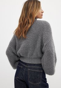 Grauer, strukturierter, kurz geschnittener Pullover mit weichem, flauschigem Finish und voluminösen Ärmeln, kombiniert mit dunklen Jeans.
