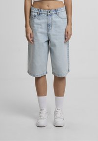 Lyseblå denim Bermuda-shorts med afslappet pasform, der har knaplukning, bæltestropper og sidelommer, kombineret med hvide sneakers og sokker.
