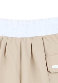 Falda beige con una cinturilla elástica blanca, cuenta con pliegues y un bolsillo lateral con una etiqueta de marca. Material de algodón suave.
