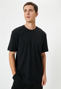 Sort kortærmet t-shirt lavet af blødt materiale, med rund hals og en brystlomme. Løs pasform og ensartet design.