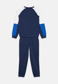 Survêtement bleu marine avec des manches longues en blocs de couleurs blanc et bleu royal, élastiques aux poignets, vu de dos.