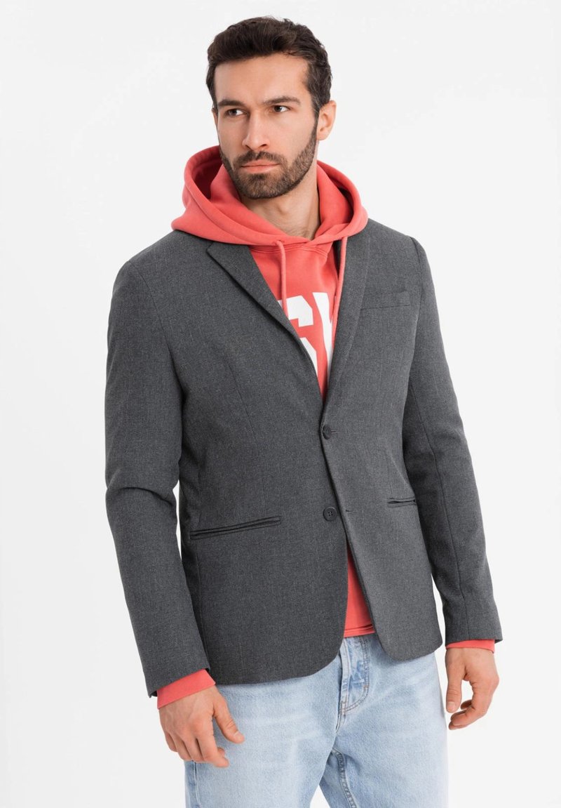 Grauer Blazer aus strukturiertem Stoff, mit einem Knopfverschluss, zwei frontalen Taschen, �über einem roten Hoodie getragen. Lässiger Stil.