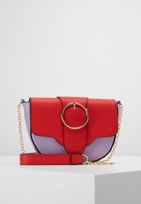 Červená a fialová kabelka přes rameno z faux kůže se zlatým kruhovým kováním, nastavitelým řetízkovým popruhem a klopou na zavírání. Výrazný design s barevným blokováním.
