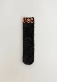 Black fuzzy sock with "Boo" in orange letters and white ghost eyes on the top edge, displayed on a plain light background.