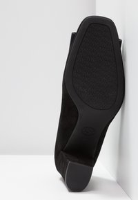 Escarpin en suede noir avec une semelle en caoutchouc texturé. Le design présente un bout pointu et une large base stable pour le soutien.