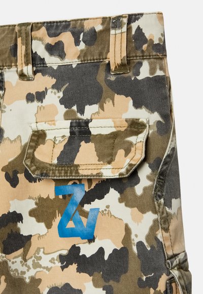 Bermudas cargo camufladas em bege, castanho e verde com um logo azul; apresentam bolsos com aba e um tecido resistente em mistura de algodão.