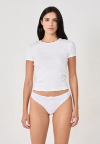 Maglietta bianca a maniche corte abbinata a uno slip bianco con pizzo, dotata di un piccolo dettaglio ricamato rosa e un fiocco decorativo.