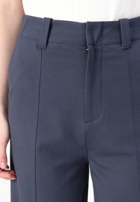 Navy blue tailored pants made of a smooth fabric, featuring a slim fit, subtle front seams, and a waistband with belt loops.