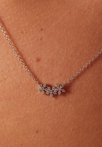 Zilveren ketting met een bloemenontwerp, versierd met kleine heldere edelstenen in een clusterarrangement, rustend tegen de huid.