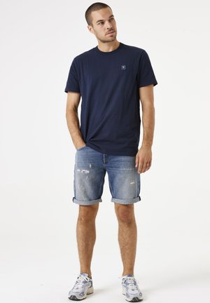 T-shirt in cotone blu navy con scollatura rotonda, abbinato a pantaloni shorts in denim azzurro con risvolti e leggere rotture.