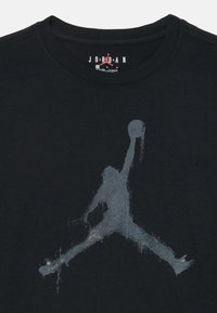 Zwarte katoenen t-shirt met een ronde hals en een vervaagde grijze grafiek van een springend figuur die een basketbal vasthoudt, gecentreerd op de voorkant.