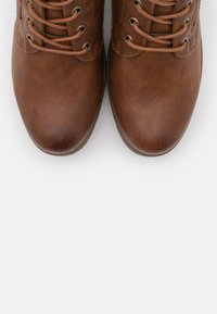 Bottes en cuir marron avec des bouts ronds, un design à lacets et des œillets en métal ronds. Surface légèrement texturée, arborant une finition lisse.