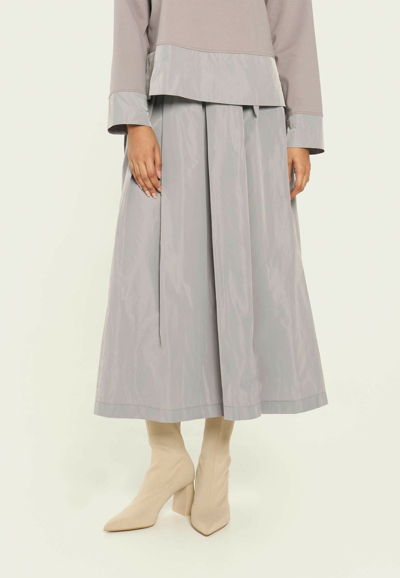 Falda gris con pliegues hecha de material ligero, combinada con botines crema. La falda tiene una textura suave y un detalle de cinturilla ancha.