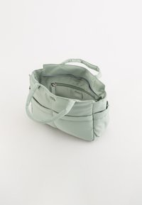 Helles grünes Tote-Bag aus weichem Material, mit zwei Griffen und einer inneren Reißverschlusstasche. Es zeichnet sich durch eine glatte Textur und ein schlichtes Design aus.