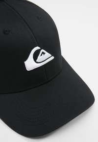 Svart baseballcap laget av bomullsblanding, med en hvit brodert logo på fronten. Glatt tekstur med en buet skjerm.