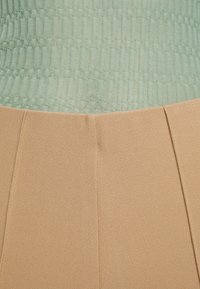 Two-piece outfit featuring a textured mint green top and beige, smooth fabric bottom with pleats. Simple, modern design.