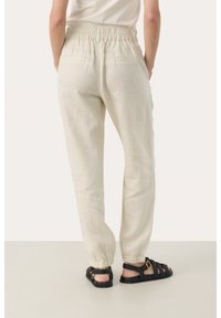 Jasno beżowe spodnie lniane z elastycznym pasem, zwężanymi nogawkami i tylnymi kieszeniami. Połączone z czarnymi plecionymi sandałami.