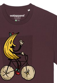 Bordeaux katoenen T-shirt met een gele bananenkarakter op een fiets, zwarte lijnen en ronde crème-kleurige wielen met details.