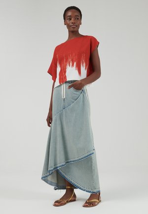 Rood en wit kleurblok t-shirt met korte mouwen, gecombineerd met een asymmetrische lichtblauwe denim maxi-rok. Model draagt platte gouden sandalen.
