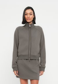Γκρι αθλητικό φούτερ με φερμουάρ και ψηλό γιακά, με ριμπ μανσέτες, συνδυασμένο με μια ταιριαστή φούστα, με λεία και απαλή υφή υφάσματος.