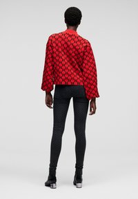 Red quilted jacket with black logo pattern, long sleeves, and a crew neck, paired with dark patterned skinny pants and black heeled boots.