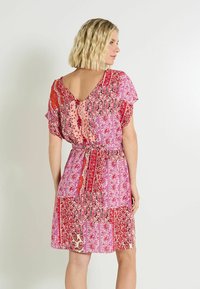 Vestido de manga corta con un diseño de espalda en V, que presenta coloridos patrones florales y de cachemira en tonos rosa, rojo y crema, ceñido en la cintura.