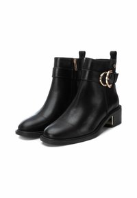 Botas de tobillo de cuero negro con punta redondeada, cremallera lateral y un acento circular dorado en la correa. Tacón bajo tipo bloque. Textura suave.