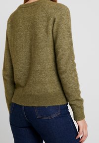 Suéter de punto verde oliva con cuello redondo, dobladillo y puños acanalados, con una textura suave y mangas raglán.