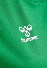 Maillot de sport vert en tissu lisse avec un logo blanc comportant un design d'abeille et le mot "hummel," situé sur la zone de la poitrine.