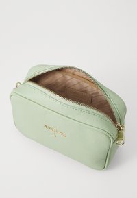 Borsa cosmetica in pelle verde menta con cerniera dorata e logo. L'interno presenta un motivo geometrico in tonalità beige.