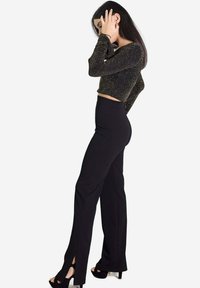 Pantalon noir taille haute avec fentes sur les côtés, associé à un top noir à manches longues court et scintillant. Tissu lisse avec détails brillants.