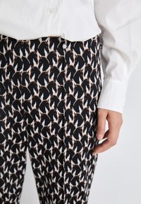 Black and white patterned pants featuring a horse motif, made of textured fabric, with a visible button closure and flat front design.