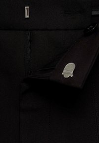 Pantalon en tissu noir avec une poche zippée, un petit accent en métal argenté et une texture lisse avec des détails ajustés.