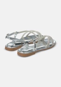 Silberne flache Sandalen mit metallischem Finish, mit überkreuzten Riemen, die mit kleinen Strasssteinen verziert sind, und einem verschließbaren Knöchelriemen.