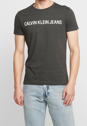 Czarny bawełniany t-shirt z krótkim rękawem i okrągłym dekoltem. Na przodzie duży biały napis "CALVIN KLEIN JEANS".