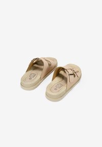 Chanclas deslizantes beiges con correas cruzadas, plantilla texturizada y detalles de yute trenzado. Presentan acentos metálicos. Suela de goma para tracción.