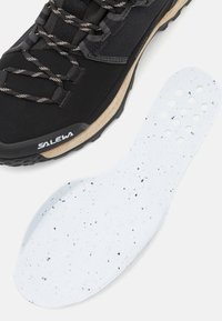 Black hiking shoe with textured surface and laces features; a white insole with black speckles beside it, highlighting both components.