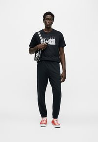 Μαύρο μπλουζάκι με γραφικό "Converse All Star", σε συνδυασμό με μαύρο παντελόνι και κόκκινα χαμηλά αθλητικά παπούτσια. Περιλαμβάνει μικρή μαύρη τσάντα με λεπτομέρεια αστέρι.