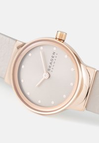 Round wristwatch with a rose gold case, light gray dial, and dot markers. Features a textured light gray leather strap and a crown.