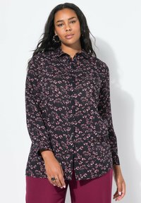Camicia nera con bottoni, motivo floreale rosa, maniche lunghe e colletto, abbinata a pantaloni bordeaux. Tessuto di texture liscia.