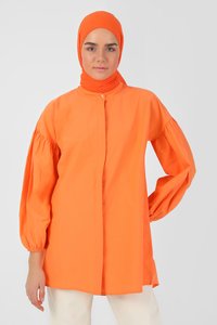Blusa di cotone arancione con maniche lunghe a sbuffo, colletto alla mandarina, bottoni frontali e vestibilità comoda. Abbinata a pantaloni color crema.