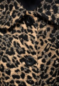 Tissu imprimé léopard avec deux boutons noirs et un col, montrant la texture et le motif détaillés du vêtement.