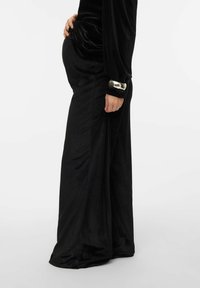 Melns, samtaina kleita ar garām piedurknēm un sakrātām detaļām. Tajā ir sudraba akcents pie piedurknes un pielāgots siluets ap vēderu.