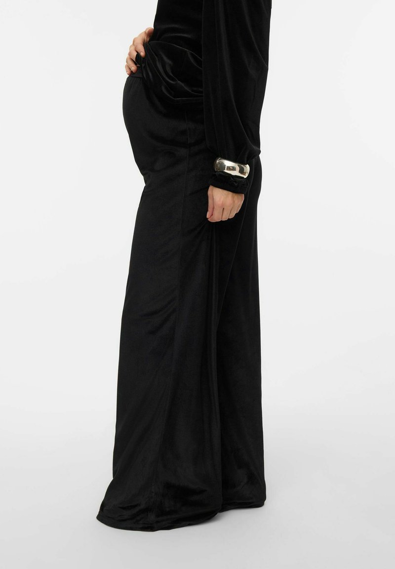 Melns, samtaina kleita ar garām piedurknēm un sakrātām detaļām. Tajā ir sudraba akcents pie piedurknes un pielāgots siluets ap vēderu.