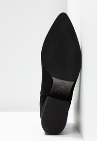 Semelle d'une chaussure noire à bout pointu avec un talon carré, montrant la semelle en cuir et un détail de marque embossé.