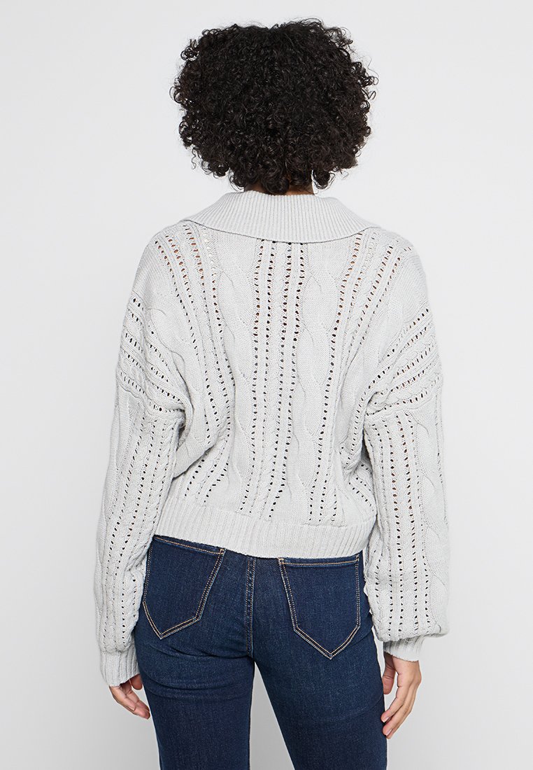 Maglione grigio chiaro a trecce, con colletto a coste, design a trama aperta e motivi testurizzati, aderente in vita e con maniche lunghe.